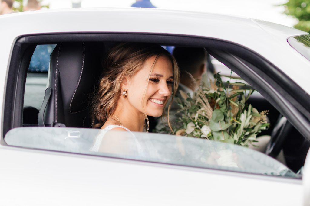 eine Frau mit Hochsteckfrisur sitzt auf dem Beifahrersitz eines Mercedes-AMG und hält einen Blumenstrauß in der Hand