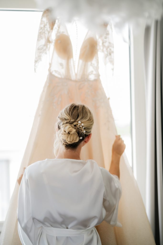 Braut steht mit dem Rücken zur Kamera und streicht über ihr Kleid.