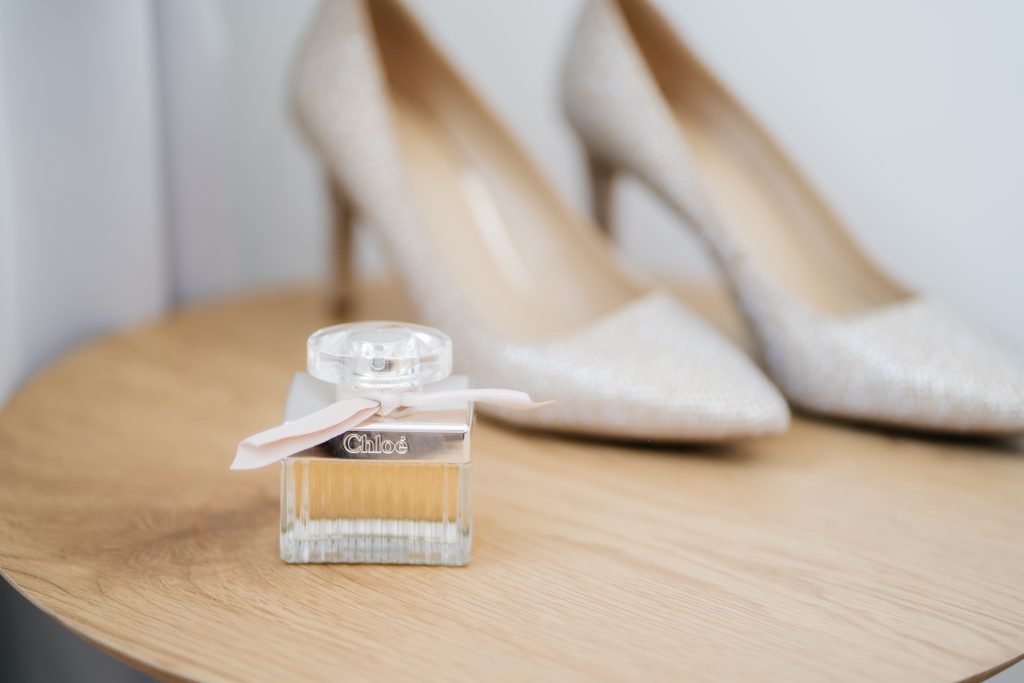 ein Paar Highheels im Hintergrund und eine Flasche Parfum stehen auf einem Holztisch.